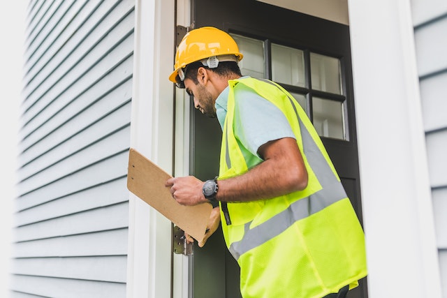 property inspector wearing a yellow hardhat and reflective vest looking at property exterior