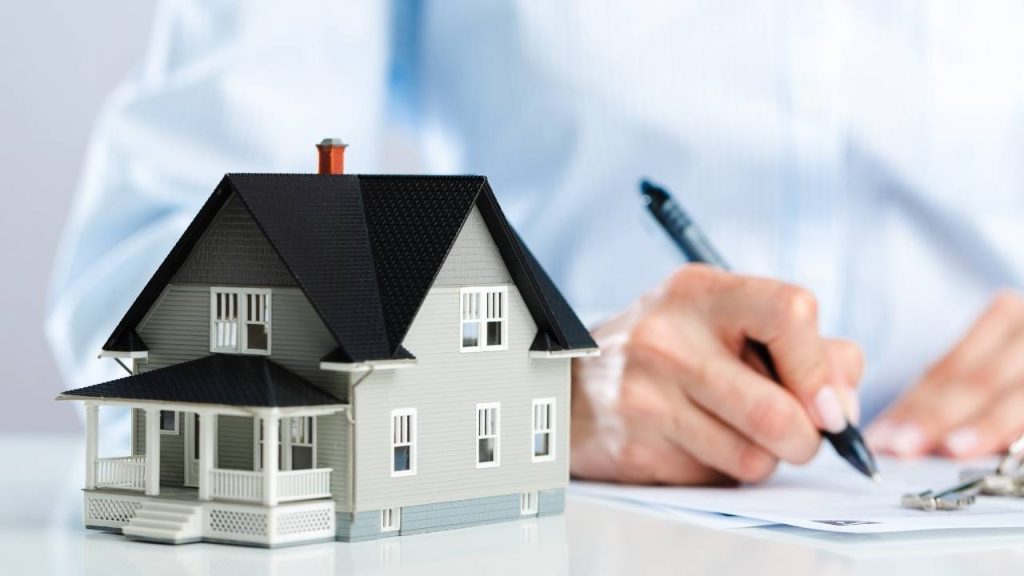 person signing something with a house figurine next to them