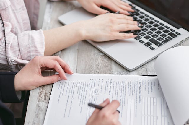 person reviewing documents beside another person on a laptop