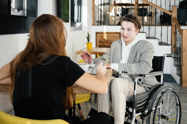 Two people sitting across from each other at a table, one is in a wheel chair