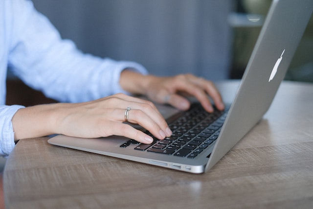 person in blue shirt writing on their laptop at a desk